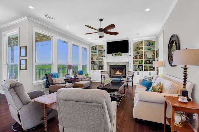 living area featuring dark wood-style flooring, visible vents, ornamental molding, a ceiling fan, and a stone fireplace