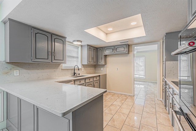 kitchen with a sink, a peninsula, decorative backsplash, and a textured ceiling