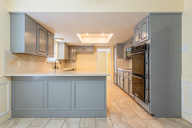 kitchen with a raised ceiling, a peninsula, gray cabinets, light countertops, and a sink