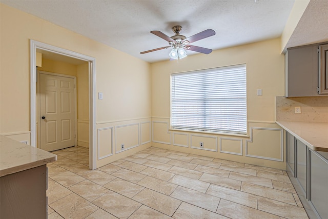 unfurnished dining area featuring a wainscoted wall, a decorative wall, a textured ceiling, and ceiling fan