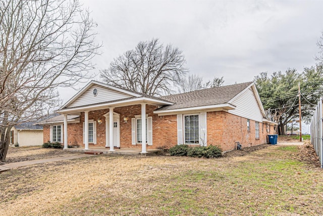 neoclassical / greek revival house featuring a shingled roof, covered porch, brick siding, and a front lawn