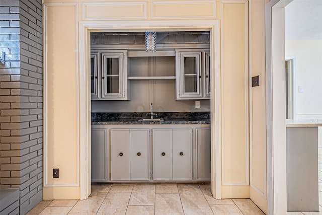 kitchen featuring light tile patterned floors, brick wall, glass insert cabinets, and dark stone counters