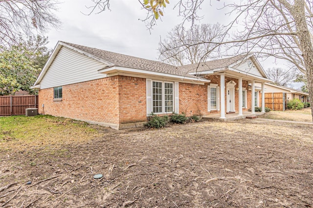 view of front of home featuring a shingled roof, brick siding, fence, and central AC