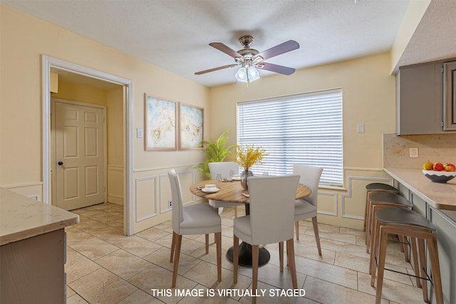 dining room with a wainscoted wall, a decorative wall, a ceiling fan, light tile patterned flooring, and a textured ceiling