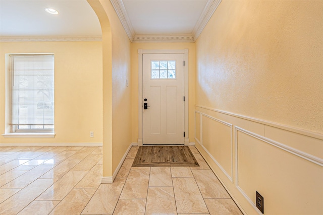 entrance foyer with ornamental molding, arched walkways, a wainscoted wall, and a decorative wall