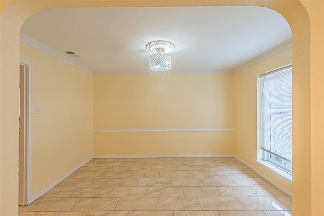 spare room featuring arched walkways, visible vents, crown molding, and baseboards