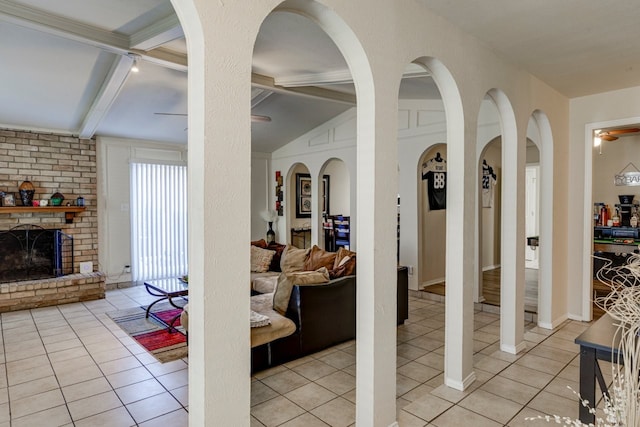 living area featuring lofted ceiling with beams, light tile patterned floors, ceiling fan, and a brick fireplace