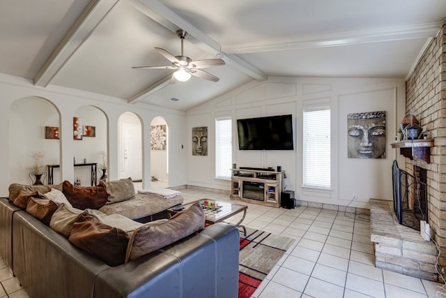 living area featuring lofted ceiling with beams, ceiling fan, light tile patterned flooring, and a brick fireplace