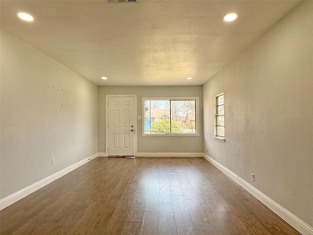 empty room with recessed lighting, wood finished floors, visible vents, and baseboards