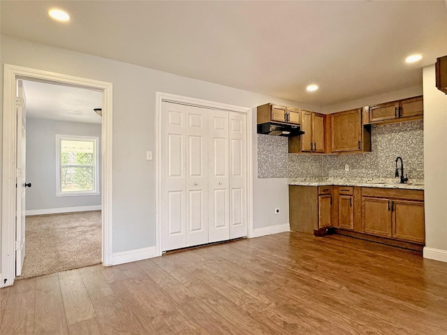 kitchen featuring under cabinet range hood, wood finished floors, a sink, brown cabinets, and decorative backsplash