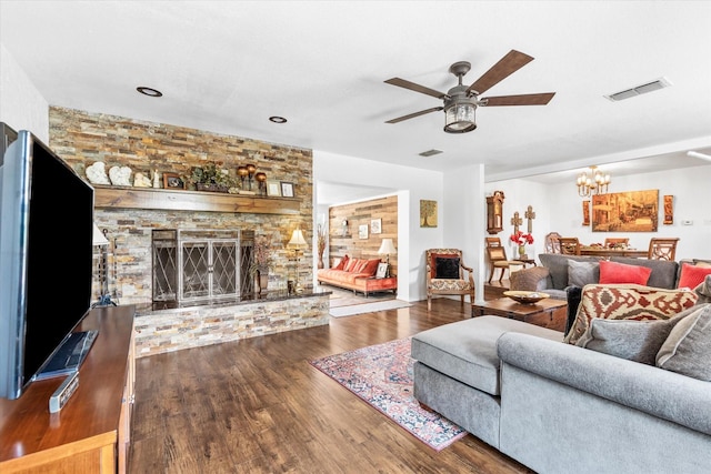 living area featuring a fireplace, visible vents, wood finished floors, and ceiling fan with notable chandelier