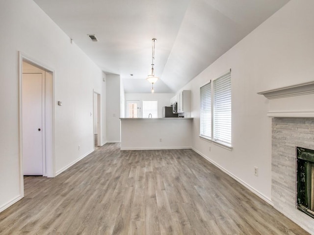 unfurnished living room featuring light wood finished floors, baseboards, visible vents, lofted ceiling, and a fireplace