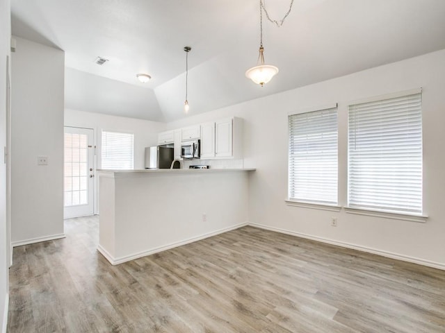 kitchen with pendant lighting, stainless steel microwave, white cabinets, a peninsula, and fridge