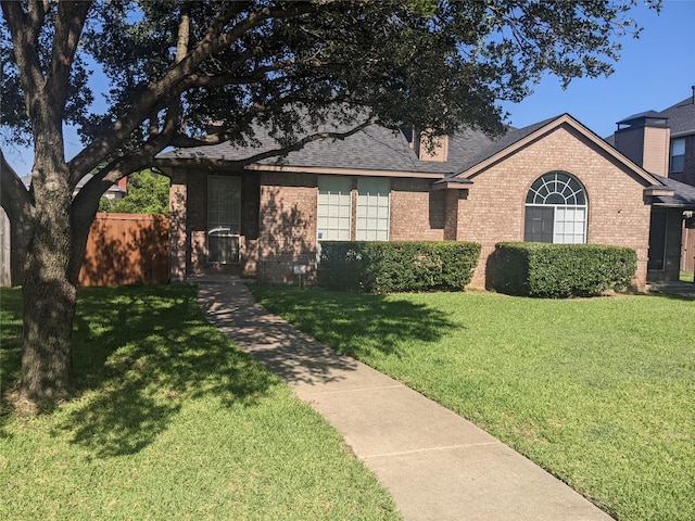 view of front of house featuring brick siding, a front yard, fence, and a shingled roof