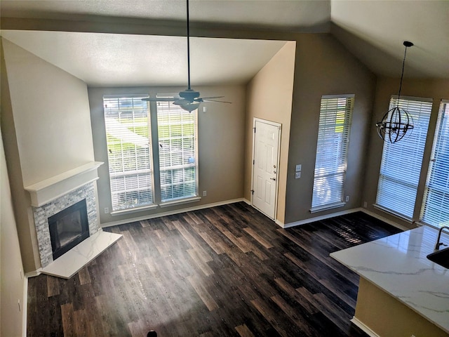 interior space featuring dark wood-style flooring, a premium fireplace, vaulted ceiling, a textured ceiling, and baseboards