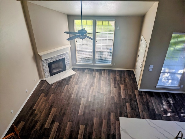 unfurnished living room featuring ceiling fan, baseboards, dark wood finished floors, and a stone fireplace