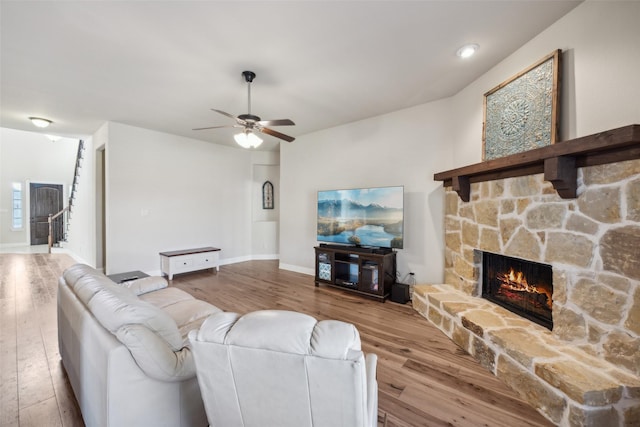 living area featuring light wood finished floors, ceiling fan, a fireplace, and baseboards