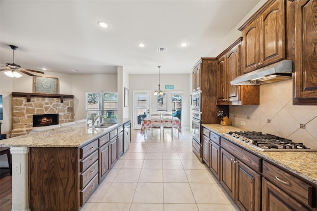 kitchen featuring decorative light fixtures, stainless steel appliances, a sink, light stone countertops, and under cabinet range hood