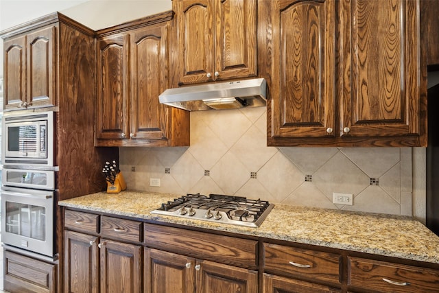 kitchen with stainless steel appliances, backsplash, under cabinet range hood, and light stone counters