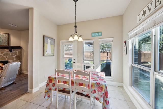 dining space featuring baseboards, visible vents, light tile patterned flooring, and a stone fireplace