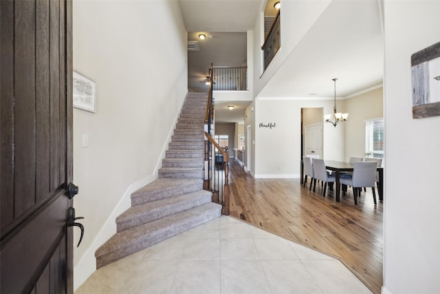 entryway with light tile patterned floors, baseboards, a towering ceiling, stairs, and crown molding