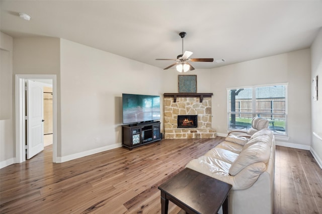 living room with ceiling fan, a stone fireplace, baseboards, and hardwood / wood-style flooring