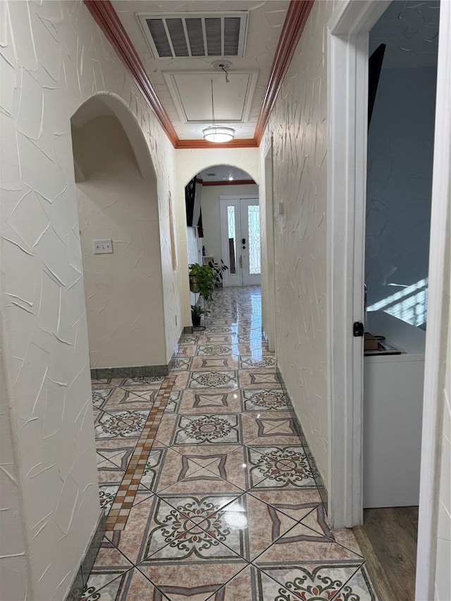 hallway with arched walkways, a textured wall, visible vents, attic access, and crown molding