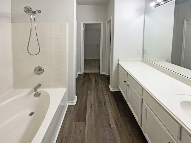 full bath with a spacious closet, washtub / shower combination, vanity, wood finished floors, and baseboards