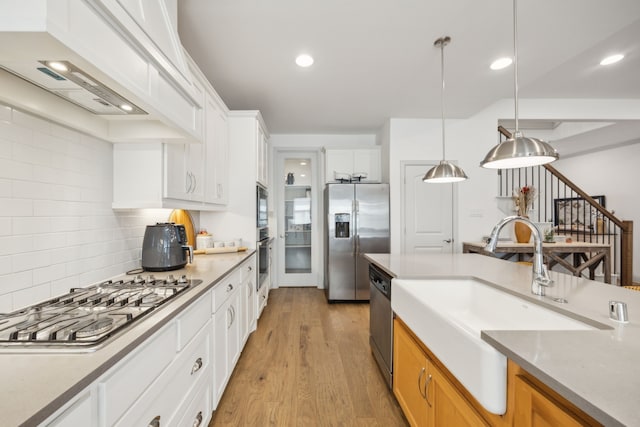 kitchen featuring light wood-style flooring, decorative light fixtures, stainless steel appliances, white cabinetry, and a sink