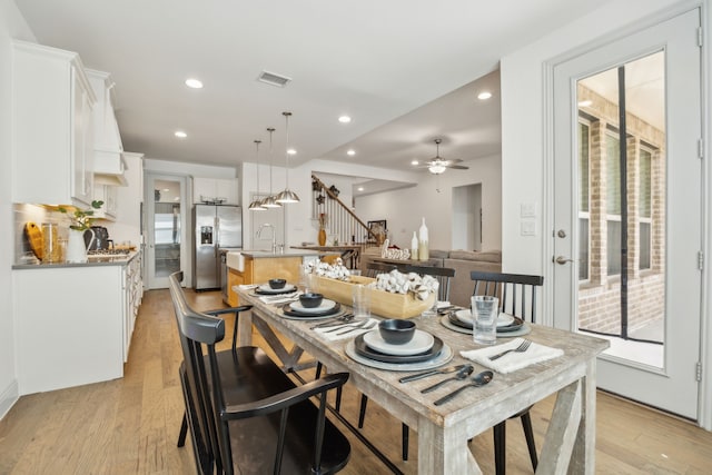 kitchen with a kitchen island with sink, white cabinets, open floor plan, hanging light fixtures, and stainless steel fridge