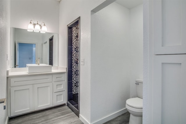 bathroom featuring toilet, wood finished floors, vanity, baseboards, and a shower