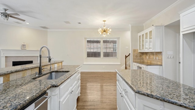 kitchen with glass insert cabinets, dark stone countertops, hanging light fixtures, white cabinetry, and a sink