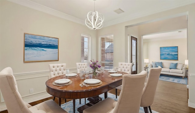 dining area with light wood finished floors, visible vents, wainscoting, ornamental molding, and a chandelier