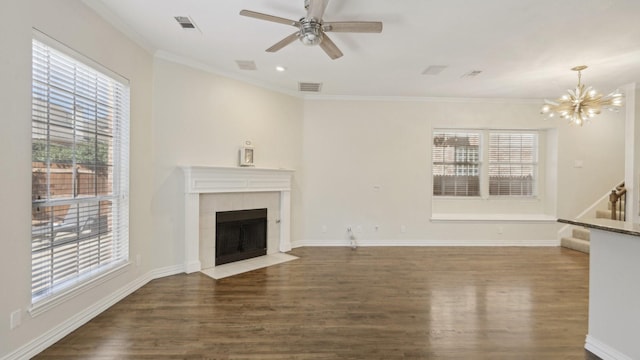 unfurnished living room featuring a tile fireplace, ceiling fan with notable chandelier, dark wood-type flooring, visible vents, and crown molding