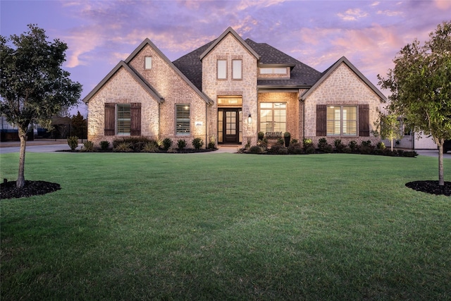 french country home with a lawn and brick siding