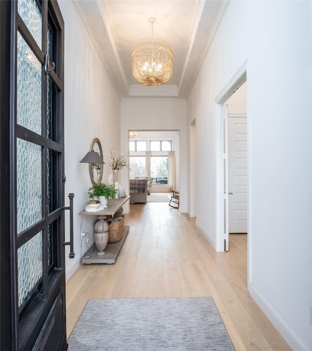 hallway with a chandelier, baseboards, light wood finished floors, a tray ceiling, and crown molding