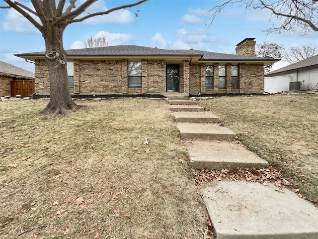 view of front facade featuring brick siding, a chimney, a front lawn, and central air condition unit