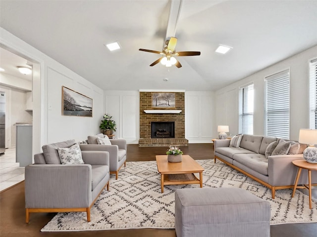 living room featuring ceiling fan, wood finished floors, vaulted ceiling, a fireplace, and a decorative wall