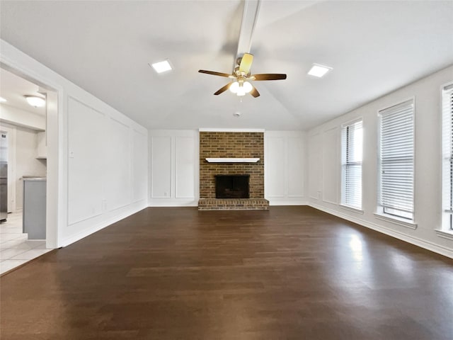 unfurnished living room with vaulted ceiling, a brick fireplace, a ceiling fan, and a decorative wall