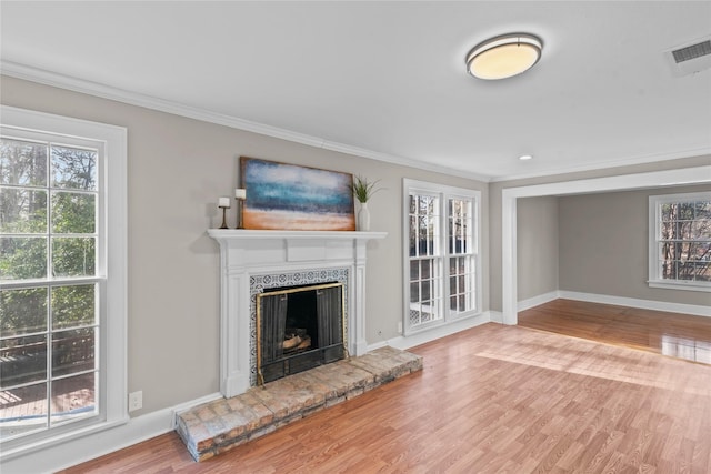 unfurnished living room with a fireplace with raised hearth, visible vents, ornamental molding, wood finished floors, and baseboards