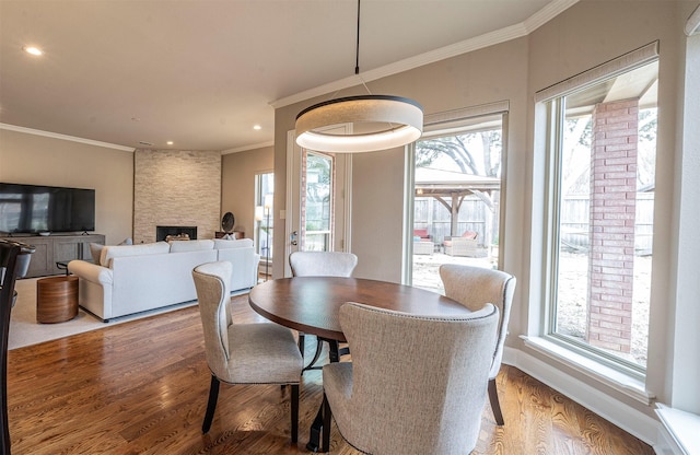 dining area featuring a large fireplace, baseboards, wood finished floors, crown molding, and recessed lighting