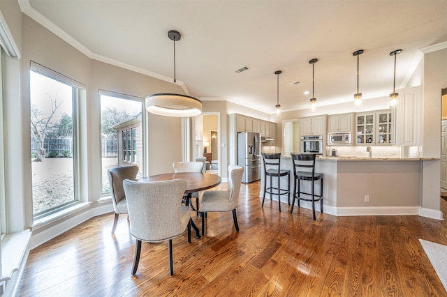 dining area with ornamental molding, wood finished floors, visible vents, and baseboards