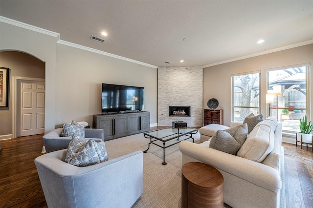 living area featuring visible vents, arched walkways, ornamental molding, wood finished floors, and a stone fireplace