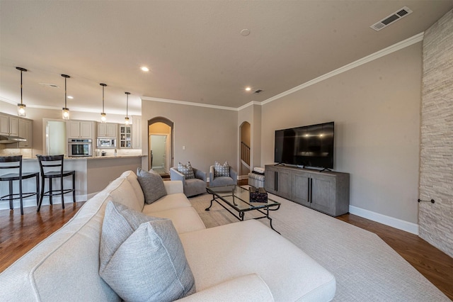 living area featuring arched walkways, crown molding, visible vents, wood finished floors, and baseboards