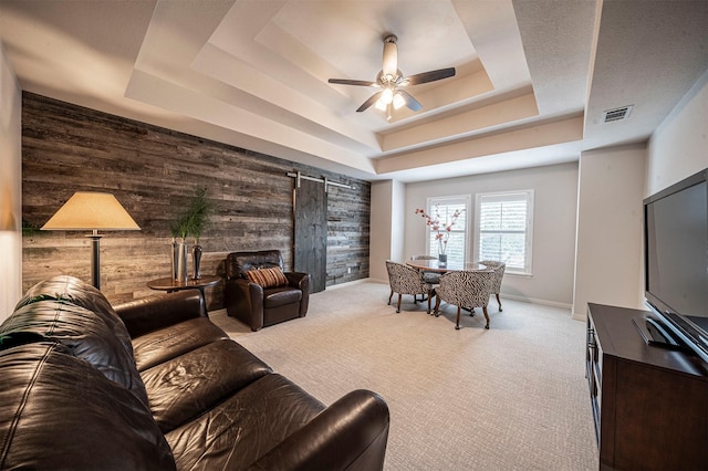 carpeted living room with ceiling fan, a barn door, wood walls, visible vents, and a raised ceiling