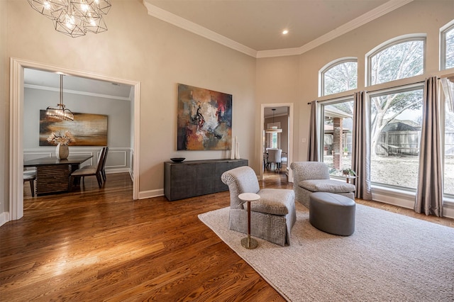 sitting room with ornamental molding, an inviting chandelier, a high ceiling, and wood finished floors