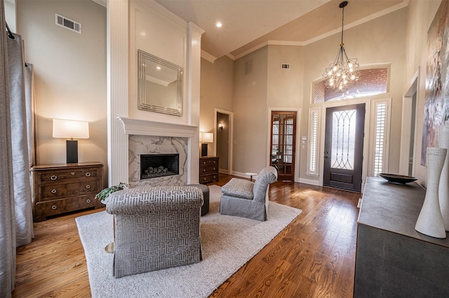 living room with baseboards, visible vents, hardwood / wood-style flooring, ornamental molding, and a high end fireplace