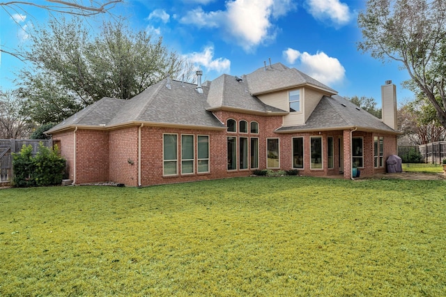 back of house featuring a yard, a chimney, fence, and brick siding