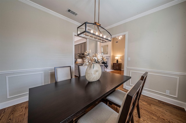 dining space with a wainscoted wall, wood finished floors, visible vents, and crown molding