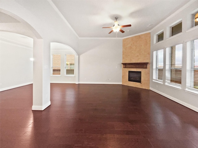 unfurnished living room with dark wood-style flooring, crown molding, ceiling fan, a tile fireplace, and baseboards